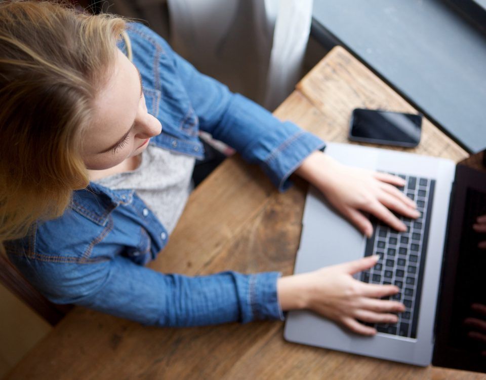 above of young blond woman working with laptop